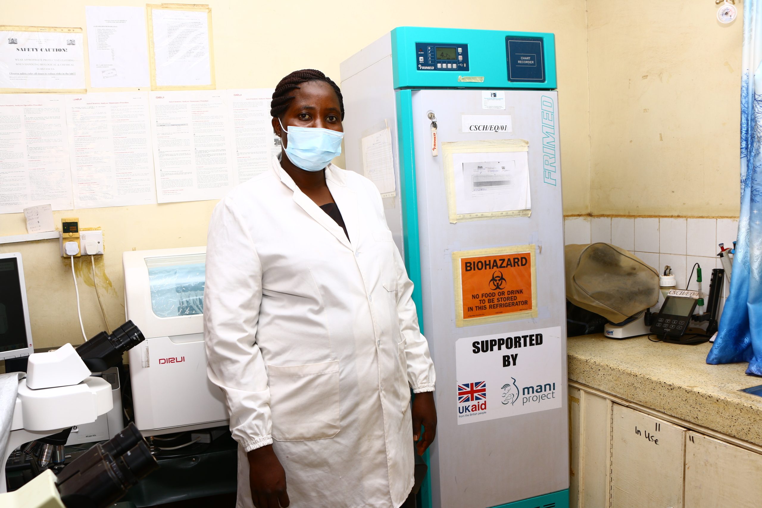 Noreen Josephs lab technologist standing by a solar powered fridge supported byt the MANI Project scaled