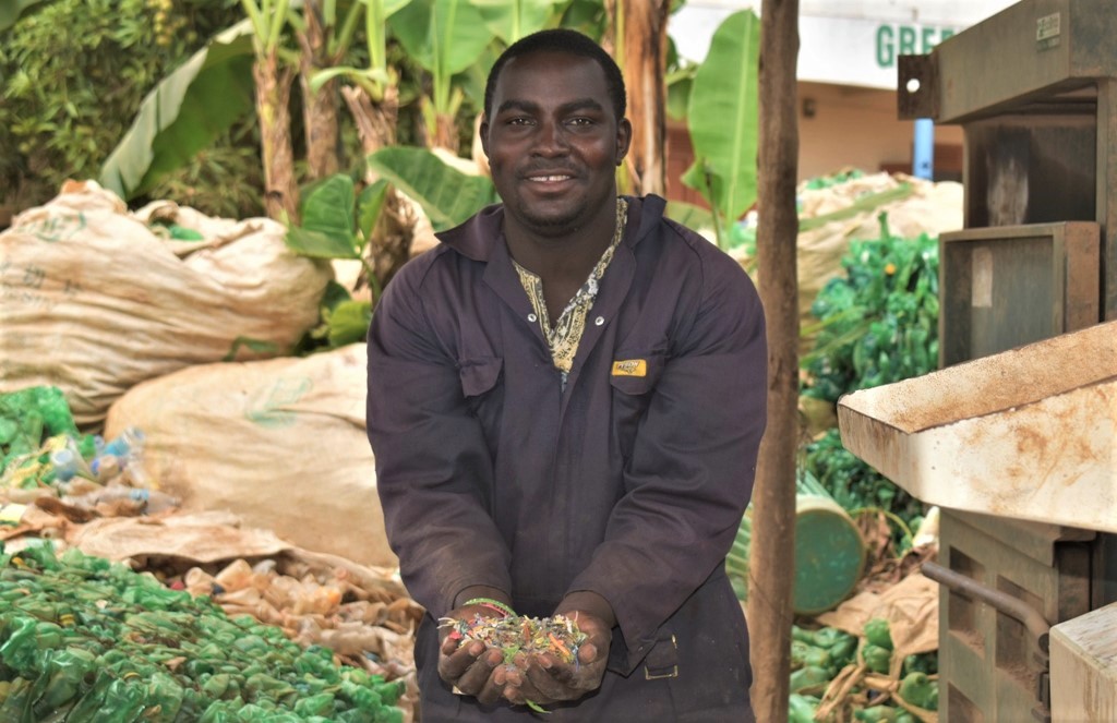 Moses Katumba a plastic pellets machine operator at Ecobrix showing pelletts used to produce plastic tiles benches fencing poles and various products.