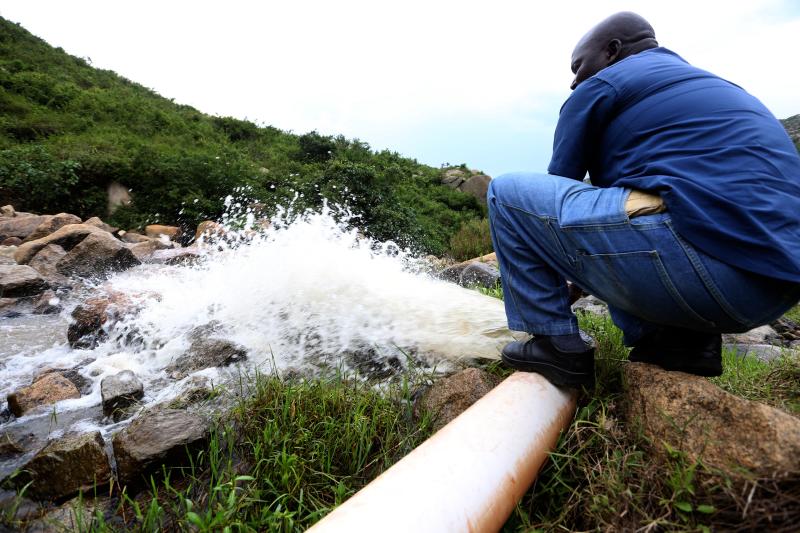 A man looks at a busted pipe along River Kibos