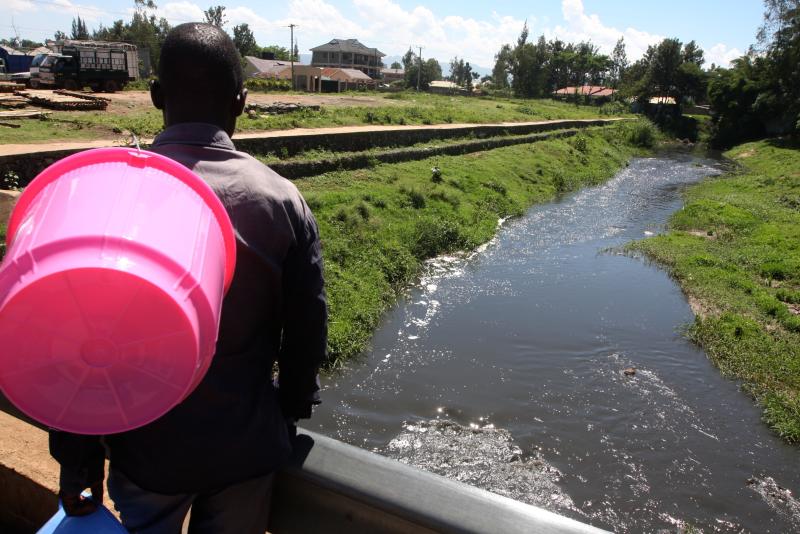 A woman stares at polluted River Auji that drains into Lake Victoria